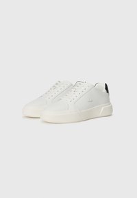Bele tene čevlje z gladkim usnjenim zgornjim delom, debelim off-white podplatom in črnim poudarkom na peti. Imajo okrogle vezalke in minimalno označevanje.