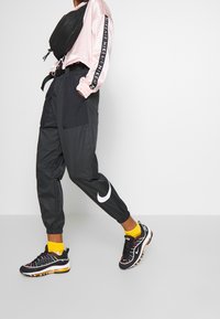 Svarta träningsbyxor med flera fickor och elastiska cuffs, i kombination med svarta sneakers med flerfärgade detaljer och gula strumpor.