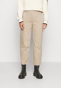 Beige katoenen broek met een getailleerde pasvorm, rechte benen en riemlussen, gecombineerd met zwarte enkellaarzen. Soepele textuur en minimalistisch ontwerp.