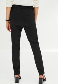 Pantalon noir sur mesure avec une taille élastique, doté de deux poches arrière, coupe slim et une texture lisse et mate.