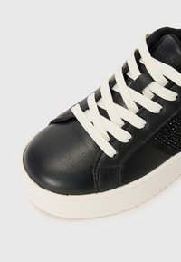 Schwarze Leder-Sneaker mit weißen Schnürsenkeln, runder Spitze, strukturiertem Obermaterial und einer kontrastierenden weißen Gummisohle. Mit Strasssteinverzierungen an der Seite.