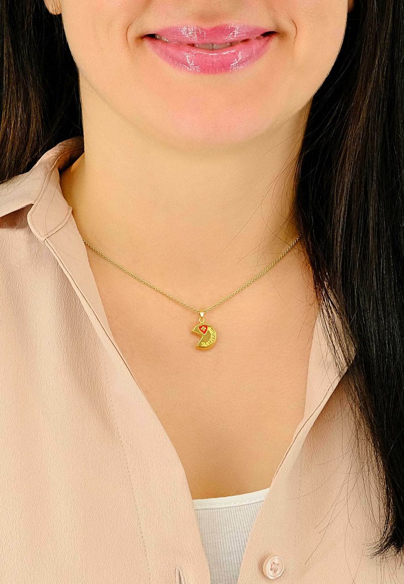 Collier en or avec un pendentif en forme de croissant de lune orné d'un accent rouge et le mot « SUNSHINE » gravé. Porté sur un haut de couleur claire.