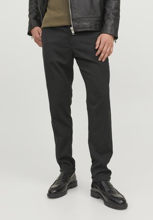 Pantaloni negri închis, croiți, cu un model subtil, slim fit, realizați dintr-un material texturat, asortați cu mocasini din piele neagră.