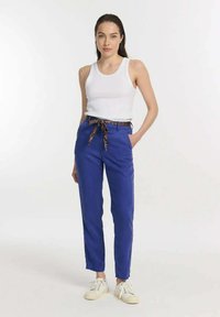 Blauwe broek met een gebonden patronenriem, gecombineerd met een witte tanktop. De broek heeft zijzakken en een rechte pasvorm.