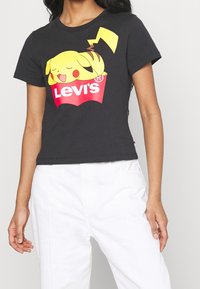 Svart bomull t-shirt med en gul Pikachu-grafik som sover på en röd Levi's-logotyp. Korta ärmar och en figurnära design.