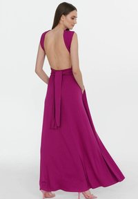 Fuchsiová maxi šaty s nízkým zadním výstřihem a širokými ramínky, které mají v pase vázací detail a splývavou siluetu. Hladká textura látky.