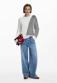 Pull blanc à côtes avec un motif rayé noir sur un côté, associé à un jean denim bleu clair à jambes larges et un sac à main rouge.