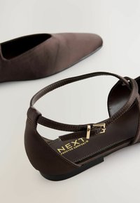 Chausson plat en tissu marron avec un bout pointu et une sangle à la cheville. Présente une boucle dorée et un design épuré, adapté pour le port décontracté.