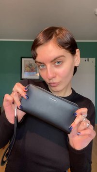 Schwarze Lederbrieftasche mit Reißverschluss und Handgelenkschlaufe. Verfügt vorne über das "Calvin Klein"-Logo. Glatte Textur mit minimalistischem Design.