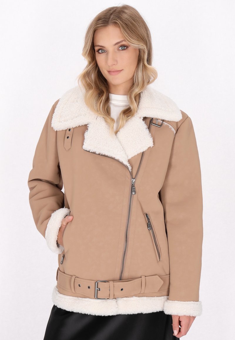 Tannfarbene Kunstlederjacke mit weißem Schafwollkragen, Reißverschluss vorne, Seitentaschen und Gürtel in der Taille. Strukturierte Oberfläche und übergroßes Design.