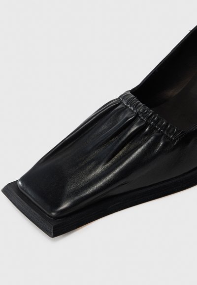 Black leather shoe with a square toe, gathered upper detail, and flat sole on a white background.