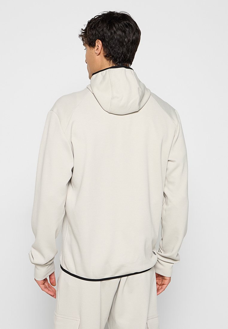 Felpa beige chiaro con cappuccio regolabile, maniche raglan e dettagli neri a contrasto in fondo, realizzata in un morbido tessuto testurizzato.