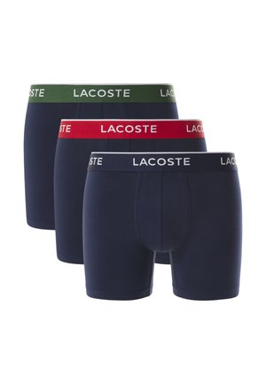 Tři páry pánských boxerek v námořnické modři. Každé má kontrastní pásky v zelené, červené a bílé barvě s logem "LACOSTE". Materiál je směs bavlny.