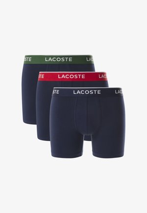 Tre par herre-bokser i navy. Hver har kontrasterende elastikker: grøn, rød og hvid med "LACOSTE" logo. Blød bomuldsblanding.