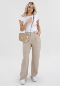 Pantaloni beige in lino a vita alta, aderenti in vita, abbinati a una maglietta bianca a maniche corte e a una piccola borsa a spalla beige con dettagli dorati.