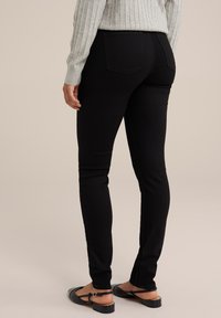 Melni slim fit džinsi, izgatavoti no denim, ar standarta jostasvietu, diviem aizmugures kabatām un pieguļošu dizainu. Kombinēti ar melnām čībām.