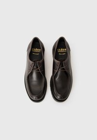 Een paar donkerbruine leren veterschoenen met ronde neuzen, met merk-inlegzolen waarop "CLÉON manufacture" staat op een witte achtergrond.