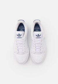Weiße Textil- und synthetische Sneakers mit niedrigem Design, Schnürverschluss, durchbrochene Details und blauen Akzenten an der Zunge und im Logo.