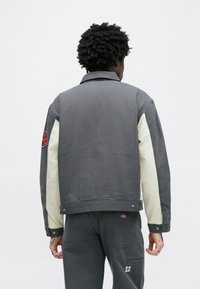 Sivá džínsová bunda s krémovými rukávmi, so zapínaním na gombíky, vyšívaným detailom na ruke a textúrovanou látkou.