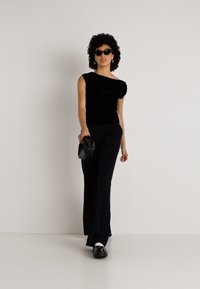 Μαύρη σατέν μπλούζα με ασύμμετρο λαιμόκομμα, συνδυασμένη με μαύρα φαρδιά παντελόνια. Τα αξεσουάρ περιλαμβάνουν υπερμεγέθη γυαλιά ηλίου και μια μικρή μαύρη τσάντα.