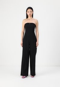 Svart strapless jumpsuit med tettsittende bodice, vide ben og en synlig glidelåsdetalj ved halsen. Myk stofftekstur.
