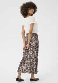 Maxi-Rock im Leopardenmuster aus leichtem Stoff, in beigen und dunkelbraunen Tönen, kombiniert mit einem weißen Kurzarmoberteil und schwarzen flachen Schuhen.