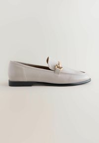 Lichtgrijze leren instappers met een spitse neus, voorzien van een gouden merkaccessoire en een slanke zwarte zool.