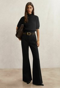 Črn pleten pulover s kratkimi rokavi, kombiniran z visokim pasom črnih širokih kavbojk, rjavim pasom in rjavo torbico na ramo.