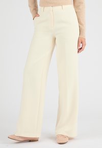 Pantaloni larghi color crema realizzati in un tessuto liscio, caratterizzati da tasche laterali e una piega discreta sul davanti.