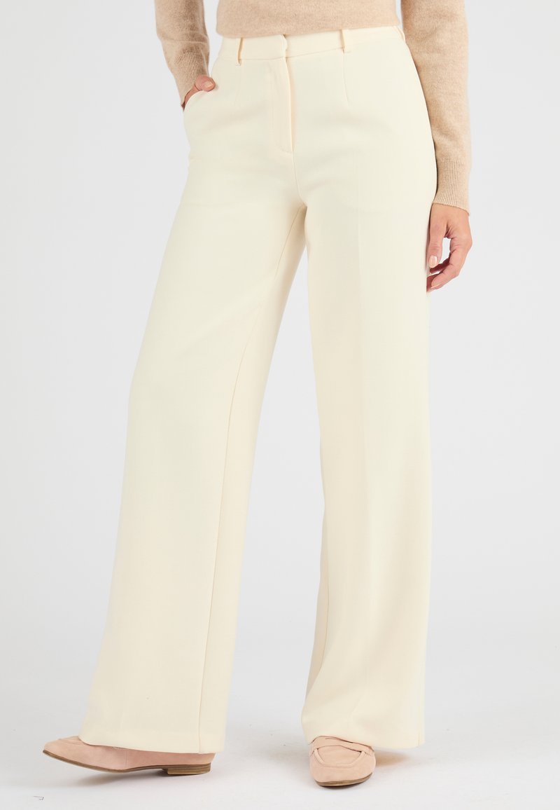Pantaloni larghi color crema realizzati in un tessuto liscio, caratterizzati da tasche laterali e una piega discreta sul davanti.