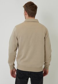 Beige mikina s vysokým límcem, žebrovanými manžetami a lemem. Hladký povrch, jednoduchý design a absence viditelných log či vzorů.