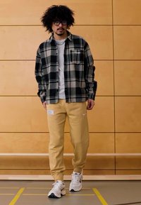 Γκρι μπλουζάκι κάτω από μαύρο και άσπρο καρό φανελένιο πουκάμισο, μπεζ φόρμα Nike με την επιγραφή "BOSTON" και λευκά αθλητικά παπούτσια.