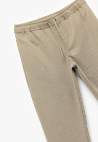 Beige jogger pants made of textured fabric, featuring an elastic waistband with drawstring and fitted cuffs at the ankles.