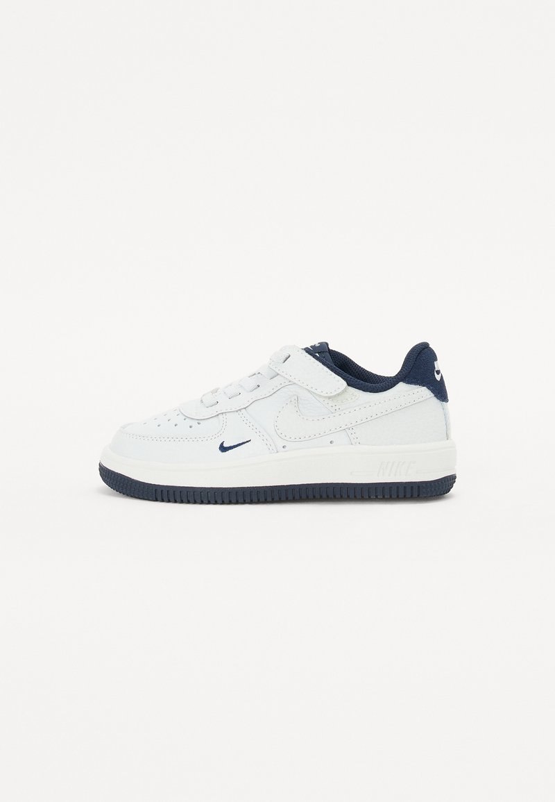 White sneaker with navy accents, made of smooth leather and textile, featuring a perforated toe box, lace-up closure, and padded collar.
