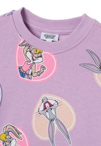Tessuto lavanda con personaggi dei Looney Tunes stampati, Bugs Bunny e Lola Bunny, all'interno di forme di cuori pastello, e un colletto a girocollo a coste.
