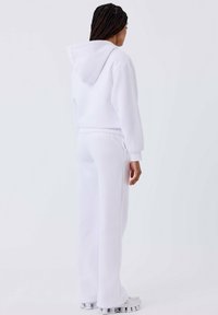 Witte hoodie en bijpassende joggingsbroek van zacht materiaal, met een ontspannen pasvorm, lange mouwen en een minimalistisch ontwerp.