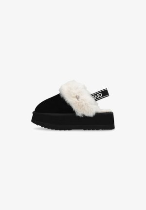 Sandale plateforme en suede noir avec une bordure en fausse fourrure blanche sur le dessus, semelle en caoutchouc noir texturé et une sangle noire avec un détail de logo.