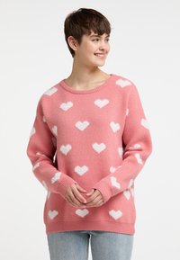 Rosa Pullover mit weißen Herzmustern, aus weichem Strickmaterial gefertigt. Besitzt einen runden Ausschnitt sowie gerippte Bündchen und Saum.