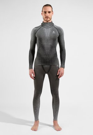 Rash guard ajusté noir et gris avec col haut, manches longues et design sans coutures; associé avec des leggings assortis présentant une texture en dégradé subtil.