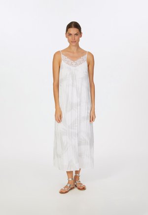 Weißes ärmelloses Maxikleid mit einer Spitzenborte, das ein graues abstraktes Muster und ein fließendes Design aufweist. Kombiniert mit silbernen Riemchensandalen.