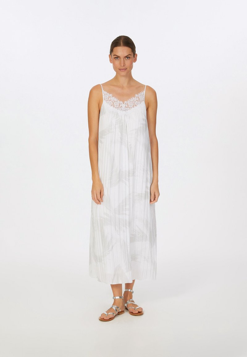 Weißes ärmelloses Maxikleid mit einer Spitzenborte, das ein graues abstraktes Muster und ein fließendes Design aufweist. Kombiniert mit silbernen Riemchensandalen.