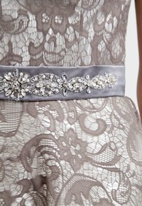 Robe en dentelle présentant des motifs floraux complexes en brun clair et crème ; une ceinture en satin gris doux ornée d'accents de cristal.