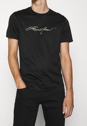 T-shirt en coton noir avec un col rond, des manches courtes et un logo en script blanc à l'avant, présentant une texture lisse et une coupe ajustée.