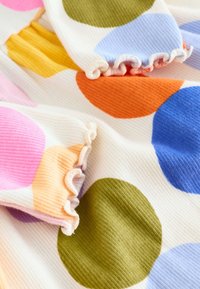 Tissu côtelé multicolore présentant de grands pois en rose, orange, jaune, vert, bleu et violet, avec des bords froncés.