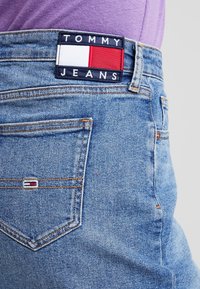 Jeans in denim blu chiaro con una vestibilità classica. Presentano un'ampia etichetta nera e rossa "TOMMY JEANS" sulla vita e un piccolo logo sulla tasca posteriore.