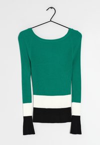 Grüner, gerippter Pullover mit langen Ärmeln, der einen breiten weißen Streifen und einen schwarzen Saum aufweist. Der Stoff hat eine strukturierte Oberfläche und die Ärmel sind eng anliegend.