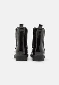 Bottines noires en cuir verni avec des panneaux latéraux élastiques, un talon texturé et des clous décoratifs le long des coutures. Semelle en caoutchouc robuste pour une bonne adhérence.