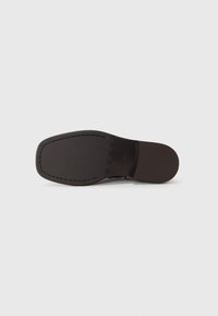 Semelle en cuir marron, surface lisse avec un bout arrondi, accents piqués le long du bord et un talon plat et rectangulaire.