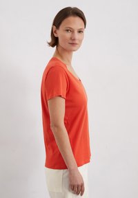 Pomarańczowy T-shirt z krótkim rękawem, z dekoltem w kształcie litery V i luźnym krojem, wykonany z miękkiego materiału bawełnianego. Gładka struktura bez widocznych wzorów.