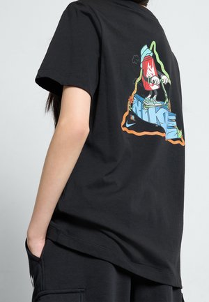 Person iført sort t-shirt med grafik af en spraymaling dåse, der kører på en løbehjul over stiliserede blå Nike-bogstaver på ryggen.
